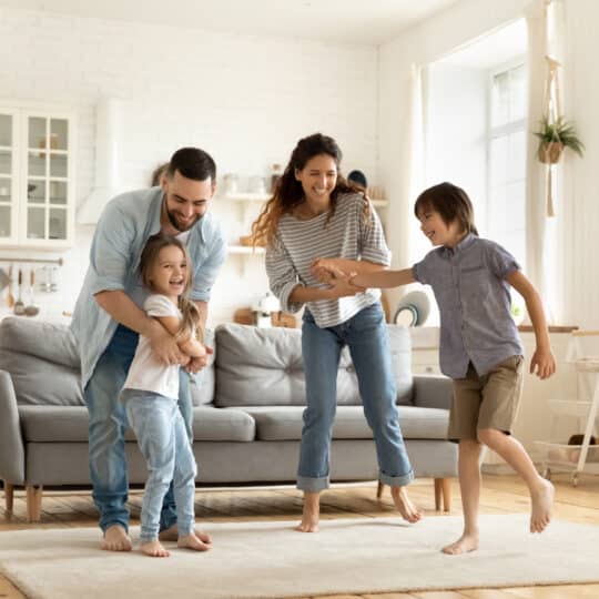 Happy family playing funny game having fun together with little son and daughter in modern living room. Young dad and mother with adorable cute children doing exercises, enjoying weekend at home.