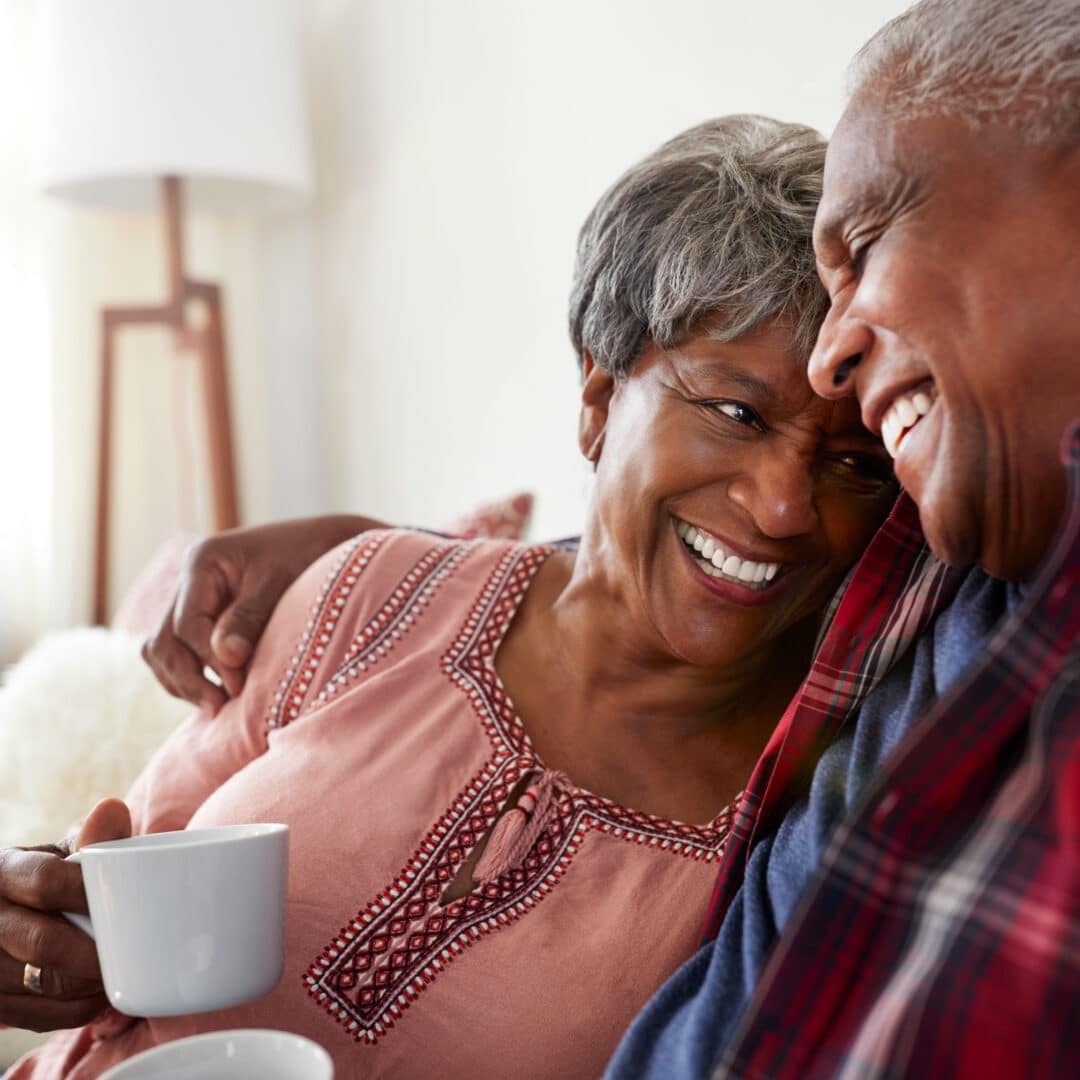 Loving Senior Couple Sitting On Sofa At Home Relaxing With Hot Drink