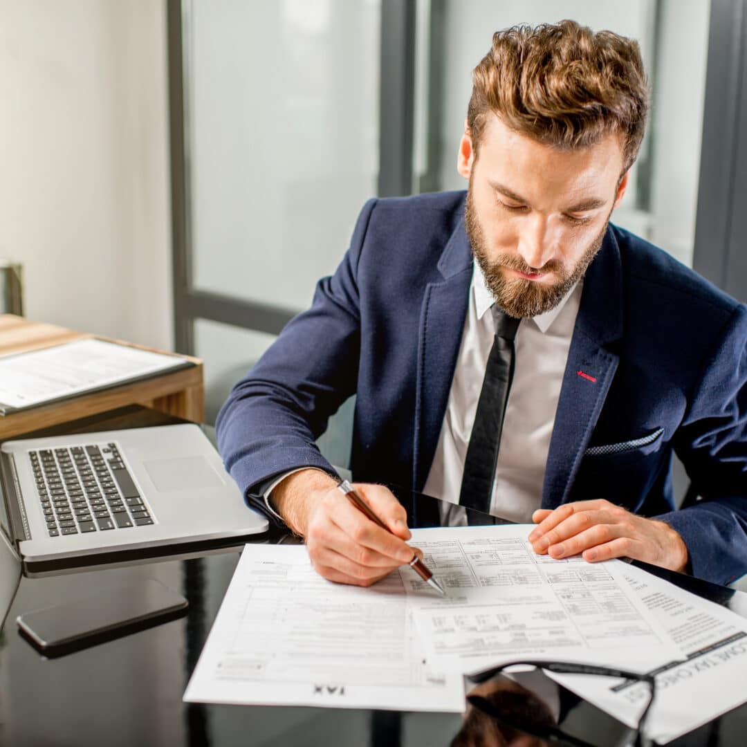 tax manager dressed in the suit working with documents and laptop at the modern office interior